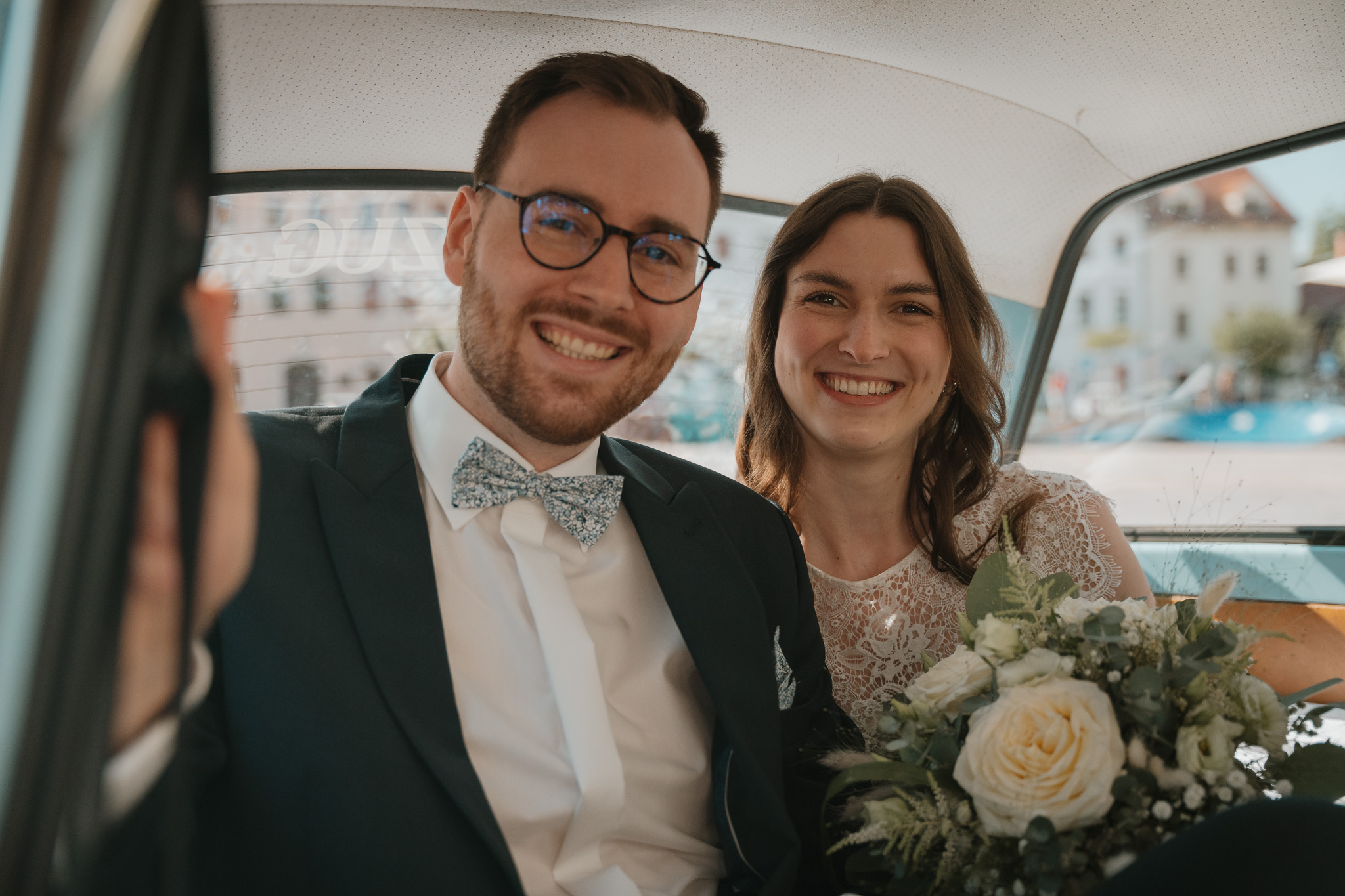 Brautpaar mit Oldtimer lacht herzlich